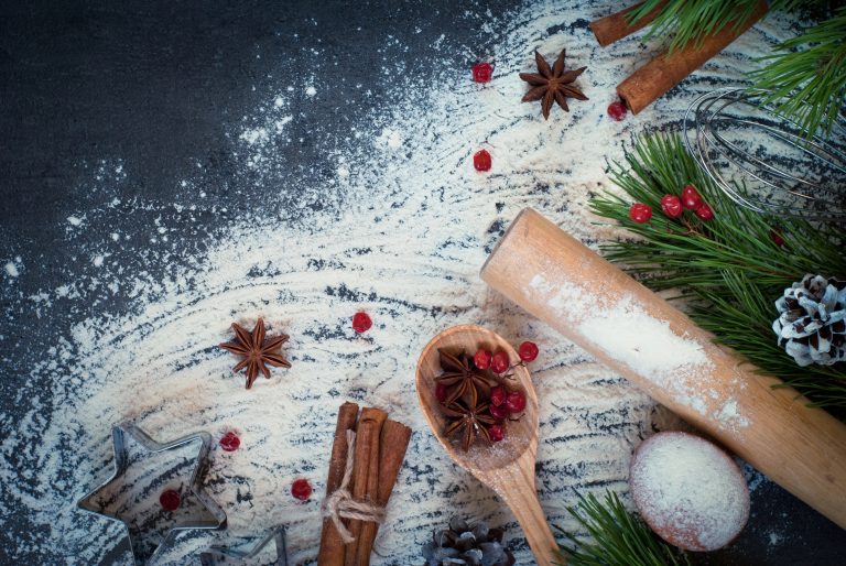 Table with messy flour, wooden spoon, rolling pin, cranberries and cinnamon sticks.