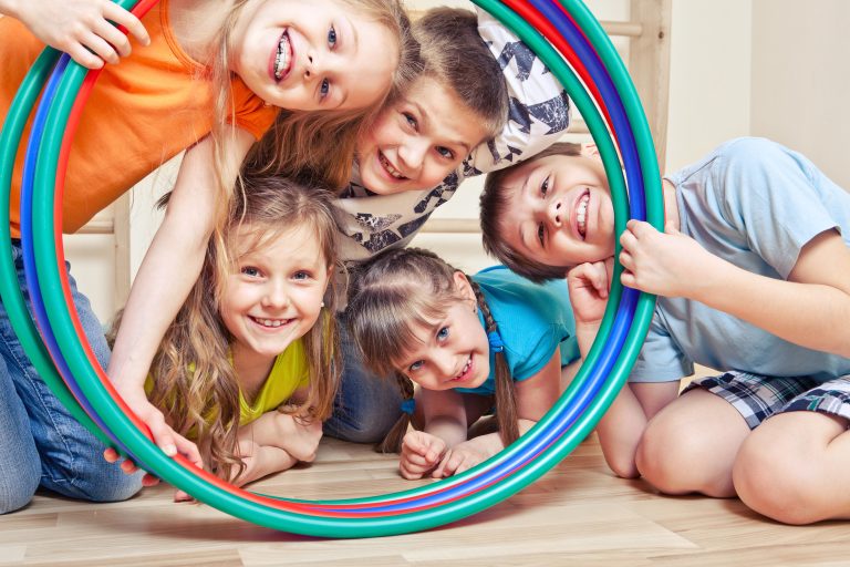 Five children on floor looking through hula hoop and smiling.