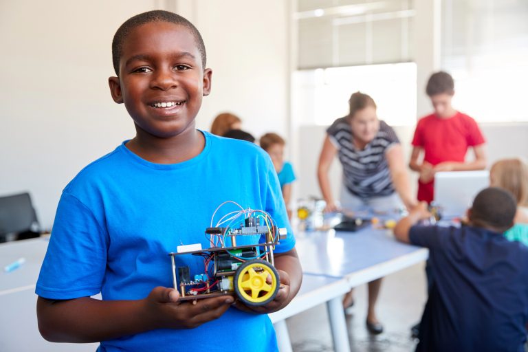 Smiling boy holding robotic device he is building at school.