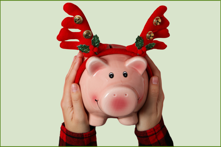 hands holding piggy bank wearing antlers adorned with jingle bells and holly