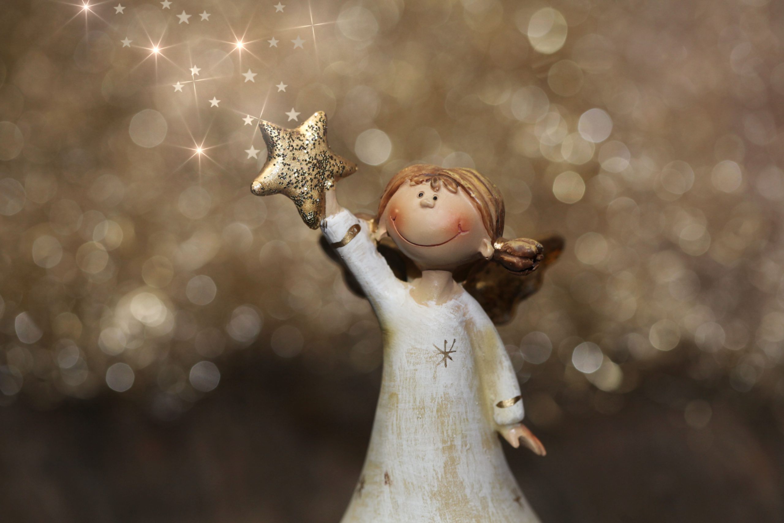 Smiling Christmas angel figurine holding a gold star in front of a gold sparkly background.